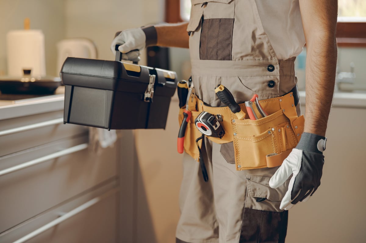 Professional handyman standing on home kitchen and holding his tool bag